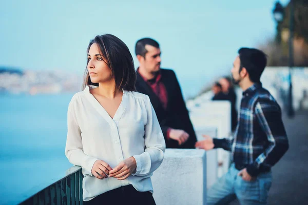 Ein schönes Mädchen steht bei Sonnenuntergang auf einer Brücke und blickt in die Ferne vor blauem Himmel und einer Abendstadt. Eine junge Frau in weißer seidenloser Bluse steht am Geländer. lizenzfreie Stockbilder