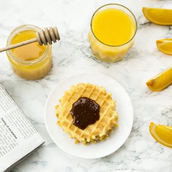Gezond ontbijt op een marmeren tafel met sinaasappelsap. lezen van een krant — Stockfoto