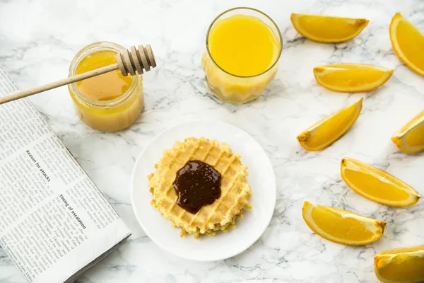 Gezond ontbijt op een marmeren tafel met sinaasappelsap. lezen van een krant — Stockfoto