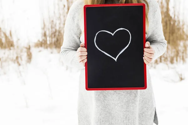 Chica en un suéter gris, sosteniendo un cartel con el corazón — Foto de Stock