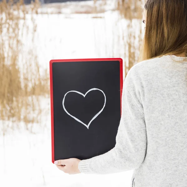 Девушка в сером свитере, держит табличку с сердцем — стоковое фото
