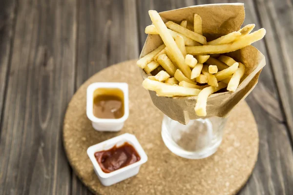 Fried potatoes and french fries in paper bags with ketchup and sweet and sour sauce — Stock Photo, Image