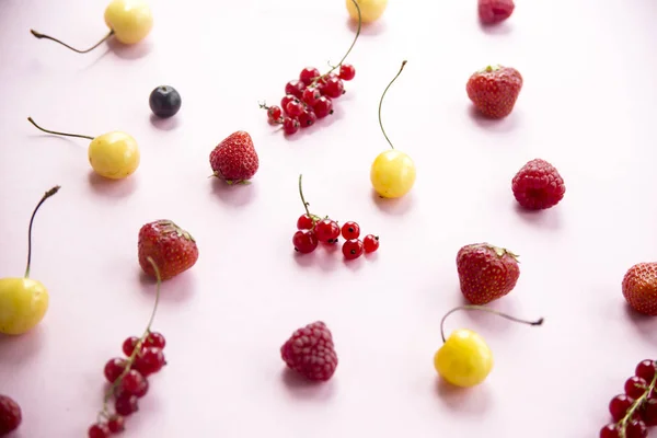 Les baies d'été sont éparpillées sur un fond rose - groseilles, cerises, framboises et fraises — Photo