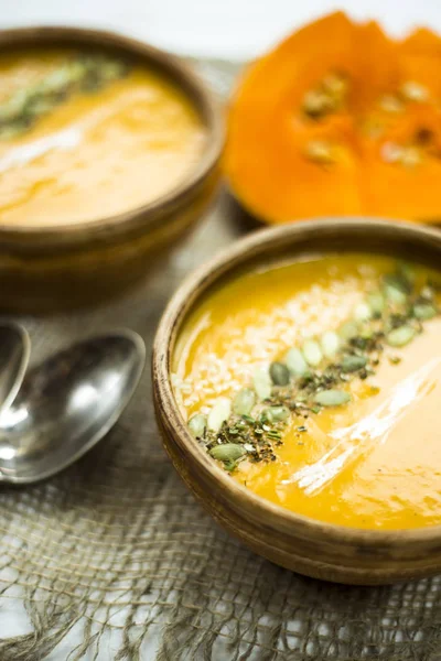 Pumpkin soup in a clay dish decorated with pumpkin seeds, sesame seeds, spices and cream — Stock Photo, Image