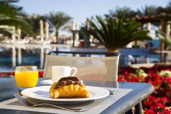 Breakfast of croissants with chocolate pasta and orange juice and coffee at the table on the terrace by the pool