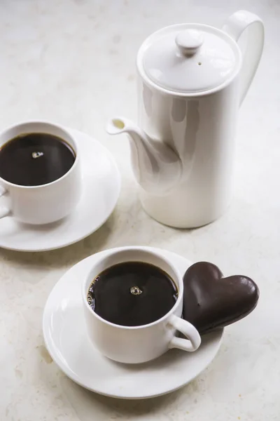 white kettle and cups on white table with chocolate heart. Minimalism and Valentine\'s Day