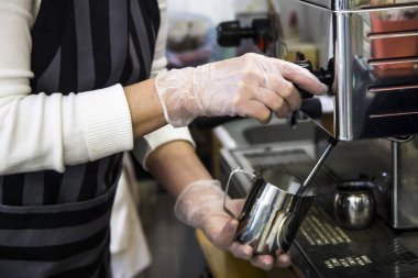 Bir kafede bir barista profesyonel kahve makinesi Kapari kullanarak bir metal kabı sütte yayıklar. Kahve evi kavramı. Cappuccino veya kahve yapma süreci