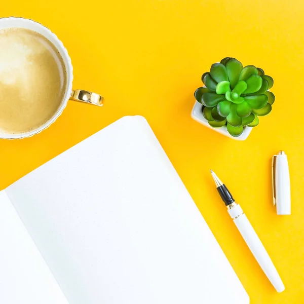 Workplace with bklonotom, pen, cup of coffee and green whiskers in white pots. On a bright yellow background. Top view. Flat lay