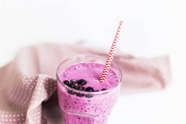 Muz Frenk üzümü smoothies pembe peçeteye speckles pipet ile yanındaki beyaz bir masada bir cam. Siyah frenk üzümü meyveleri ile yüzeyi