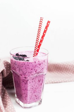 Muz Frenk üzümü smoothies pembe peçeteye speckles iki payet ile yanındaki beyaz bir masada bir cam. Siyah frenk üzümü meyveleri ile yüzeyi
