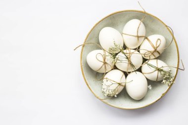 Paskalya yumurtaları minimalistically beyaz zemin üzerinde mavi bir yuvarlak tabak sicim ve gypsophila çiçeklerle dekore edilmiştir. Üstten Görünüm, düz yatıyordu. Boşaltmak