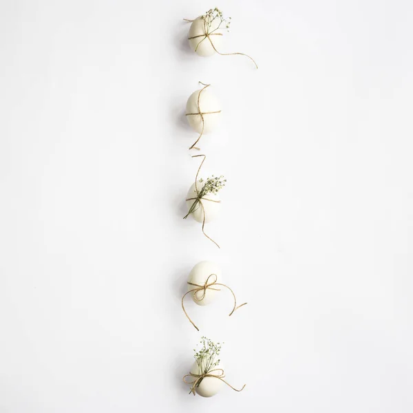 White minimalistic Easter eggs decorated with twine and flowers of gypsophila on a white background lined with a line. Easter concept. Top view, flat lay