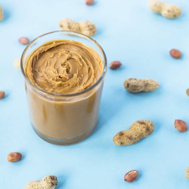 Bir cam kavanoz fıstık ezmesi yapıştırın fıstık kabuğu ve olmadan arasında ile mavi bir arka plan üzerinde. Vegan ürün. Amerikan kahvaltı