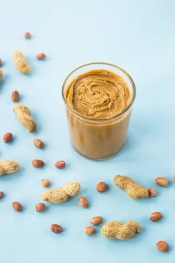 Bir cam kavanoz fıstık ezmesi yapıştırın fıstık kabuğu ve olmadan arasında ile mavi bir arka plan üzerinde. Vegan ürün. Amerikan kahvaltı