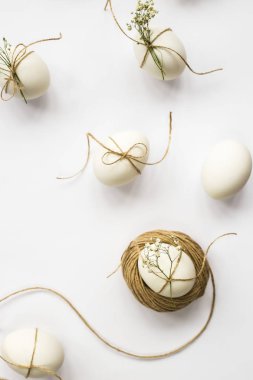 Paskalya yumurtaları minimalistically sicim ve gypsophila çiçeklerle dekore edilmiştir. Beyaz bir arka plan üzerinde kahverengi bir ip ile. Üstten Görünüm, düz yatıyordu