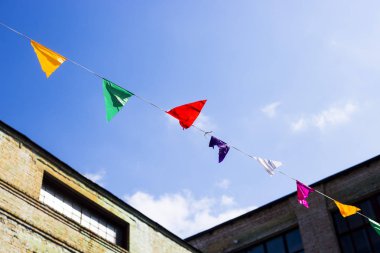 Arka plan beyaz bulutlar ile eski buildibg ve mavi gökyüzü üzerinde asılı çok renkli bayraklar dekorasyon. Boşaltmak