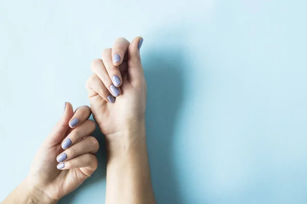 Blue manicure on female nails on a blue background. Trend for gentle pastel colors. Beauty and personal care concept