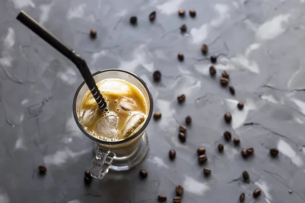 Black cold coffee with ice and milk on a gray background among the coffee beans. Summer cooling drink in a glass cup. Top view, flat lay