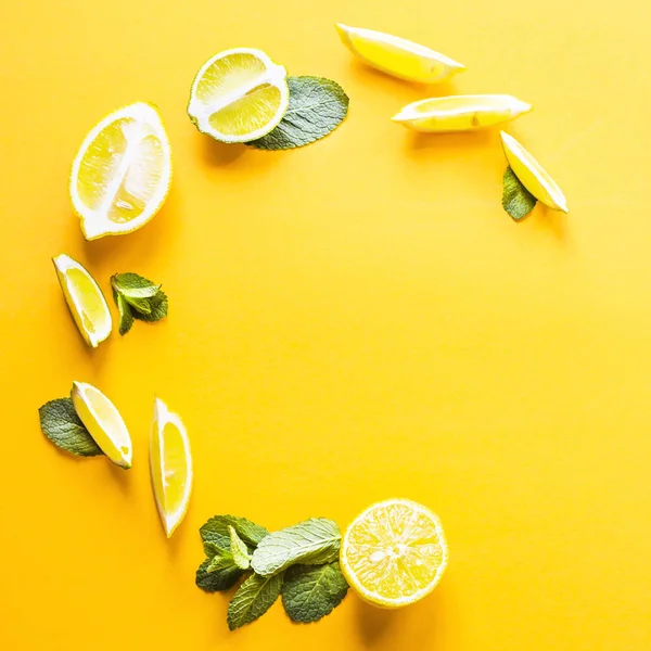 Pieces of lemon, lime and green mint leaves lined in a circle on a yellow background. Summer products for making lemonade. Top view, flat lay, copyspace