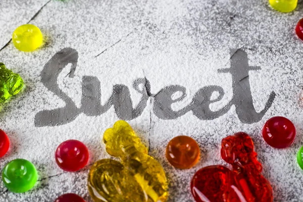 字写在灰色的具体背景上 用糖粉旁边的多色糖果和复古糖果的形式公鸡 顶部视图 — 图库照片