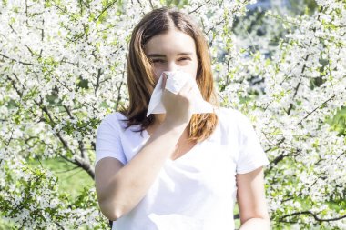 Kız bir alerji çiçeklenme sırasında yüz peçete ile burnunu siliyor. Bloom bahar ağaçlarda. Alerjik rinit kavramı