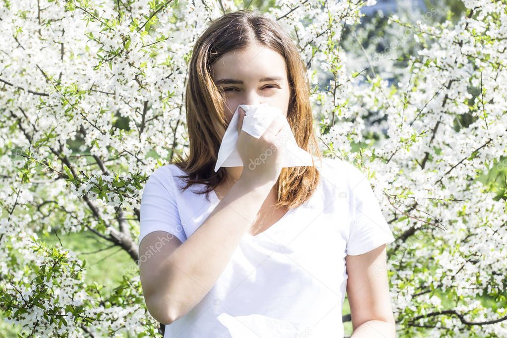 The girl wipes her nose with a facial napkin during an allergy to flowering. Spring trees in bloom. Allergic rhinitis concept