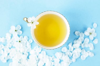 Bir mavi narin fincan yeşil çay yaprakları mavi bir arka plan üzerinde beyaz bahar çiçekli ağaçlarının arasında. Bahar ilham kavramı. Üstten Görünüm, düz yatıyordu