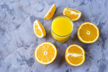Turuncu bir bardak portakal suyu yanındaki gri bir arka plan üzerine dilimlenmiş