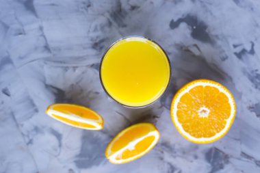 Turuncu bir bardak portakal suyu yanındaki gri bir arka plan üzerine dilimlenmiş. Üstten Görünüm, düz yatıyordu