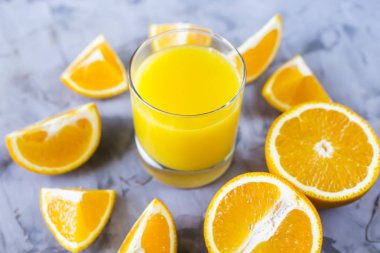 Turuncu bir bardak portakal suyu yanındaki gri bir arka plan üzerine dilimlenmiş