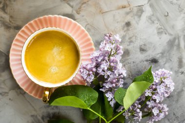 Pembe bir fincan kahve ile bir gri beton masaya Lila çiçek. Bahar kavramı. Üstten Görünüm, düz yatıyordu