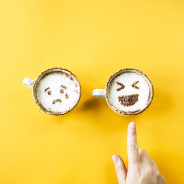 Emoji'nın kahkaha ve hüzün cappuccino kupaları üzerinde sarı bir arka plan üzerinde çizilir. Kadın kahkaha seçer. Duygular sosyal ağlar. Üstten Görünüm, düz yatıyordu