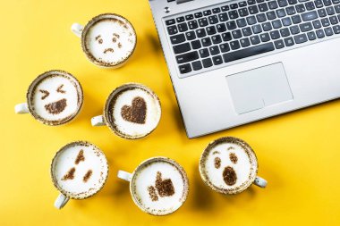 Kapuçino sarı bir arka plan üzerinde dizüstü yanında bardak boyanmış emoji gülümse. Duygu ve iletişim online kavramı