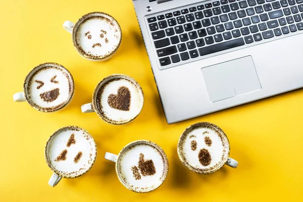 Kapuçino sarı bir arka plan üzerinde dizüstü yanında bardak boyanmış emoji gülümse. Duygu ve iletişim online kavramı