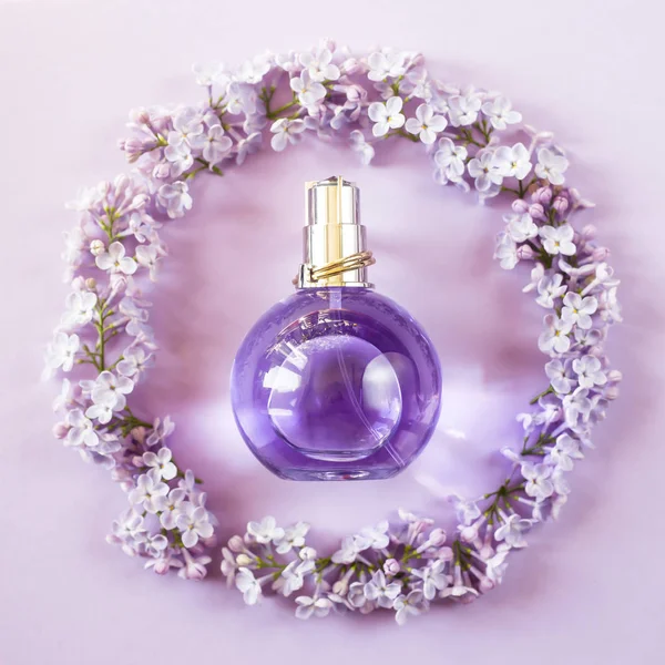 Violet bottle of women's perfume next to the flowers of lilac. Spring gentle fragrance for women. Top view, flat lay