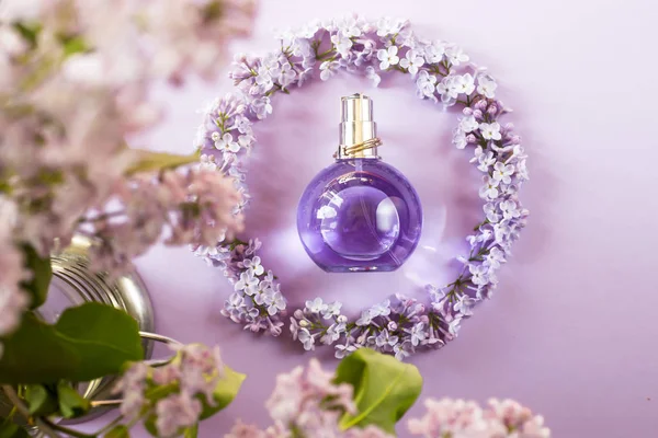 Violet bottle of women\'s perfume next to the flowers of lilac. Spring gentle fragrance for women. Top view, flat lay