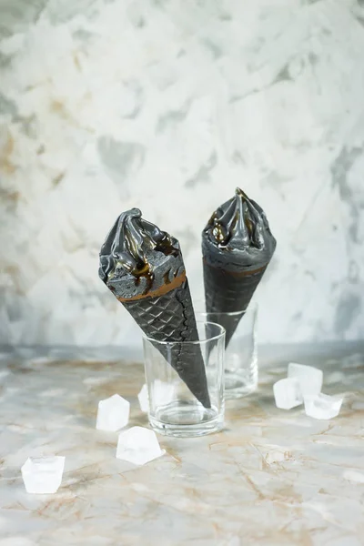 Two black ice cream in waffle cones on a gray background. Summer trend dessert