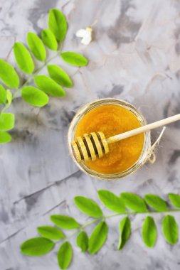 Honey from acacia and other nectar among the flowering branches of acacia. On a gray background. With a wooden spoon for honey. Top view, flat lay clipart