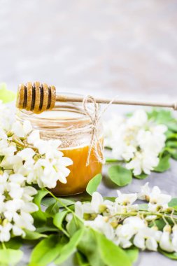 Honey from acacia and other nectar among the flowering branches of acacia. On a gray background. With a wooden spoon for honey clipart