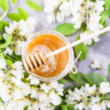 Akasya bal ve diğer nektar akasya çiçekli dallar arasında. Gri bir arka plan üzerinde. Tatlım bir tahta kaşıkla. Üstten Görünüm, düz yatıyordu