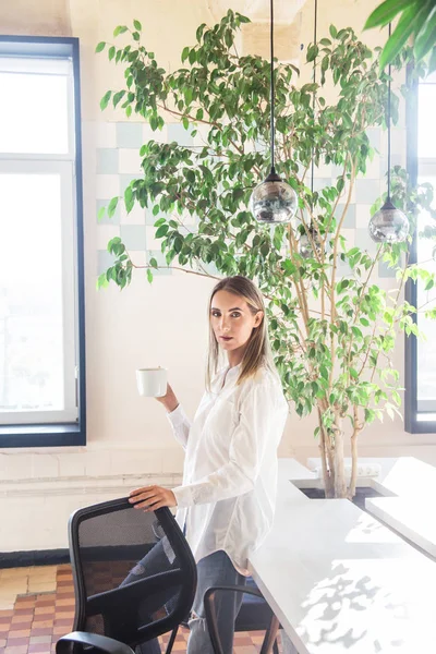 Una chica con una camisa blanca está tomando café en el descanso entre el trabajo freelancer . — Foto de Stock