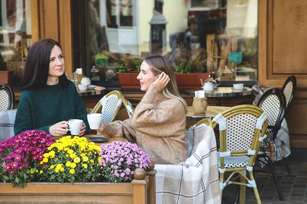 Două prietene fericite beau cappuccino într-o cafenea de stradă din oraș . — Fotografie, imagine de stoc