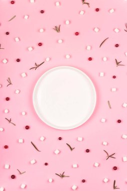 Şekerlemeler, böğürtlenler ve yeşil yapraklar arasında pembe bir zemin üzerinde beyaz boş tabak.