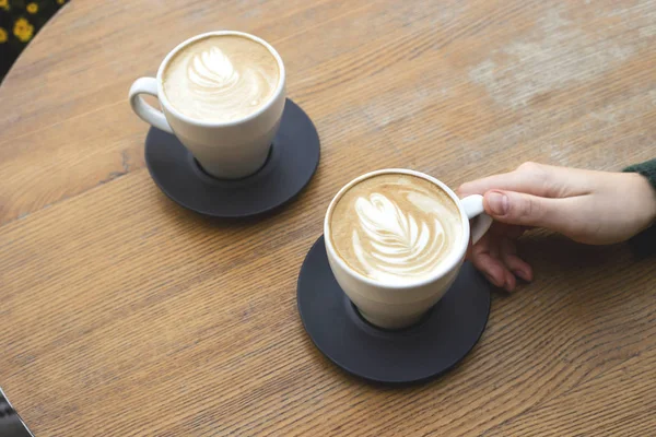 Two cups of cappuccino on a wooden table with hands of one woman. — Stock Photo, Image