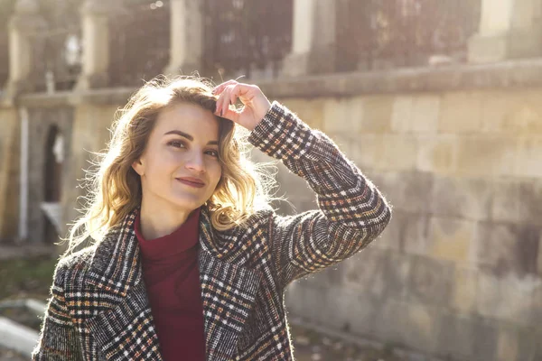 Retrato de una hermosa chica moderna con cabello rubio ondulado en abrigo de otoño a la luz del sol . —  Fotos de Stock