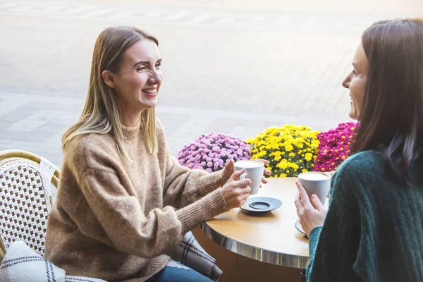 Două prietene fericite beau cappuccino într-o cafenea de stradă din oraș . — Fotografie, imagine de stoc