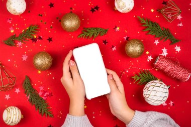 Kadın eli, kırmızı Noel süsleri arasında akıllı telefon tutar..