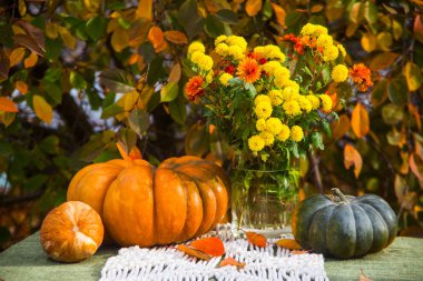 Bahçedeki masada bir buket sonbahar çiçeği ve balkabağı. Kırsal biçim.