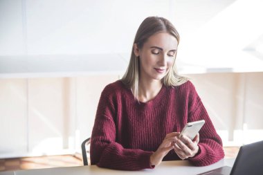 Akıllı telefondan konuşan beyaz güzel bir kız iş yerinde dizüstü bilgisayarının başında oturuyor..