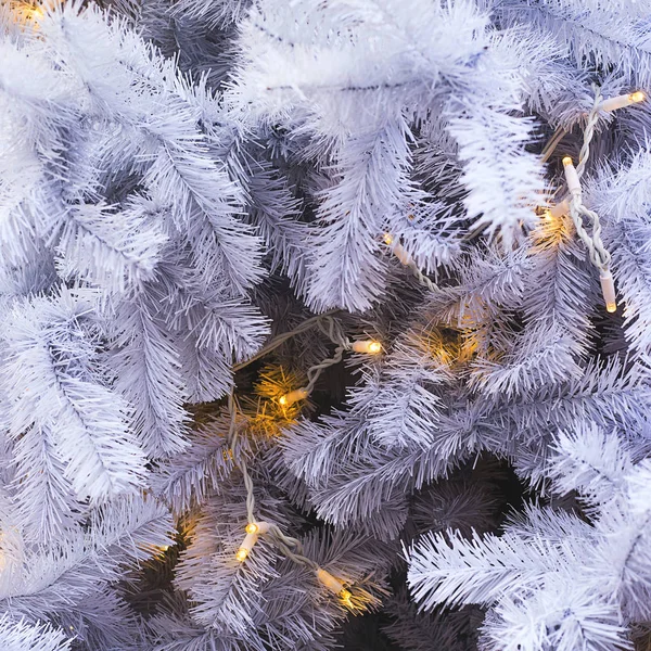 White spruce branches of an artificial Christmas tree with yellow lights. Background nd copy space. — Stock Photo, Image